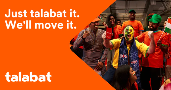 Key creative — fans in orange shirts cheer around a man with a green-and-yellow painted face who raises a phone, a man in a gray embroidered tunic at left, beside the orange panel and the talabat logo